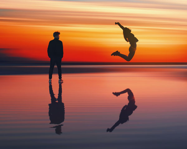 A man and woman at sunset. The woman is jumping